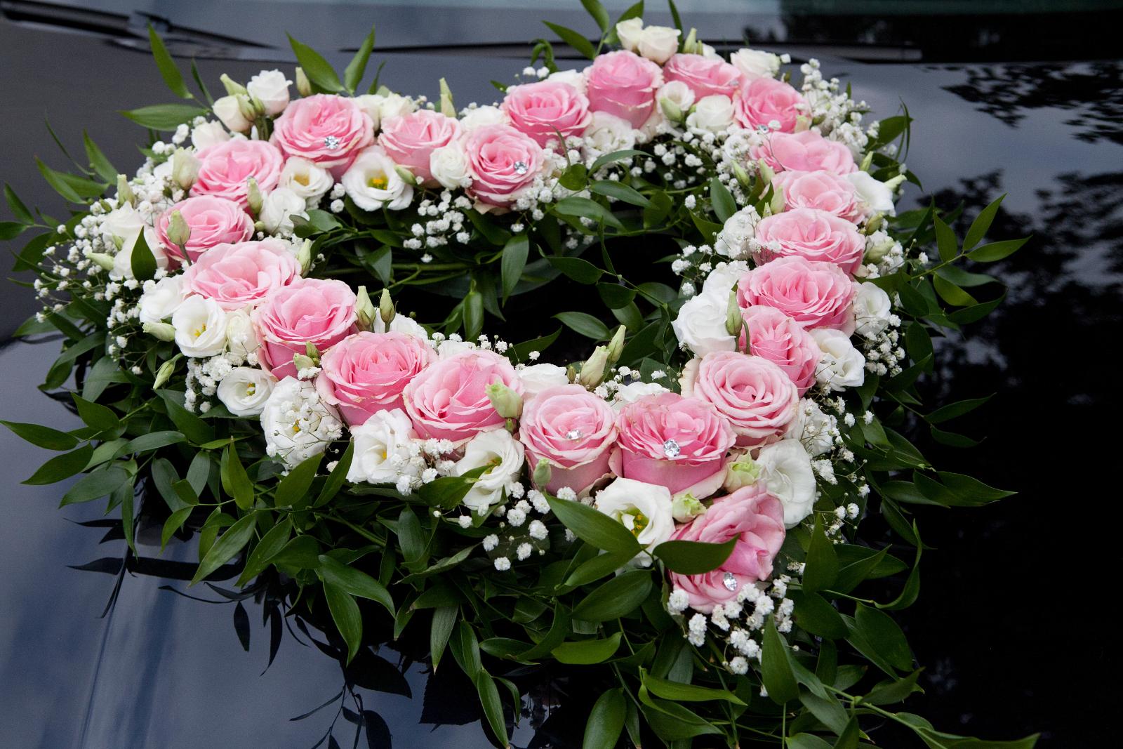 Herzförmiger Blumenschmuck aus rosa und weißen Rosen auf der Motorhaube eines schwarzen Hochzeitsautos
